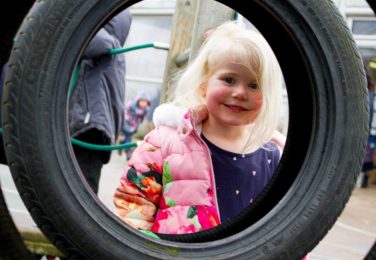 Nursery pupil smiling through playground tyre at The Lea Primary School and Nursery
