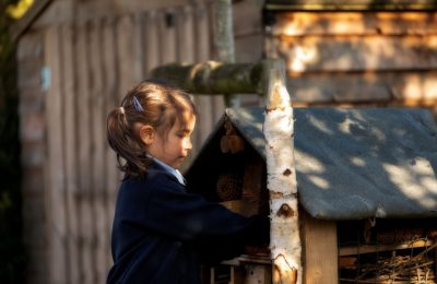 Girl pupil playing with the bug hotel at The Lea Primary School and Nursery