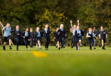 Happy pupils running across the field at The Lea Primary School and Nursery