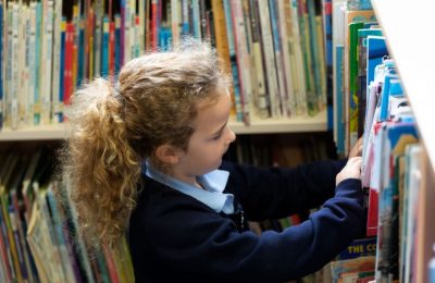 Girl pupil looking through books in the school library at The Lea Primary School and Nursery
